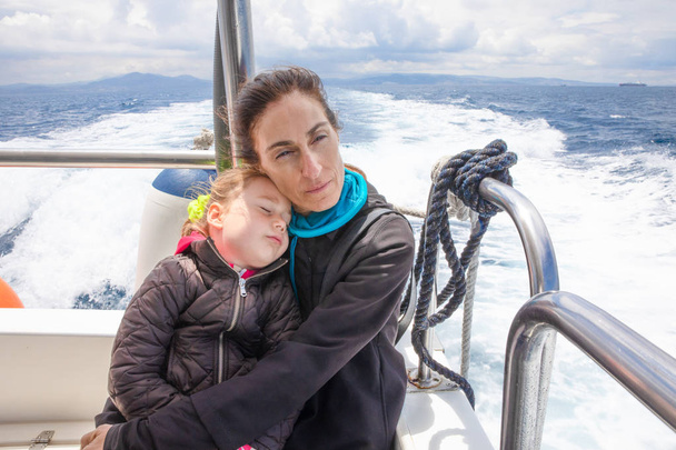 眠っている娘、4 歳の少女、ジブラルタル海峡のヨット モーター ボートの船尾に座って彼女を抱き締める女性 - 写真・画像