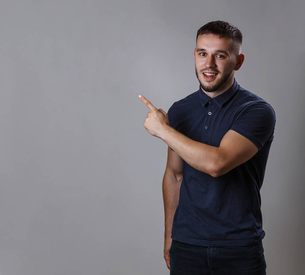 Porträt eines lustigen Mannes, der ein Hemd trägt und mit dem Finger zur Seite zeigt oder etwas demonstriert, während er auf grauem Hintergrund steht - Foto, Bild