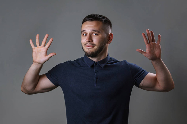 Studioporträt eines jungen Mannes, der die Hände vor sich mit dem Ausdruck "Gib auf" hochhält. das Konzept von Harmonie, Demut, Protest, humorvoller Stimmung. - Foto, Bild