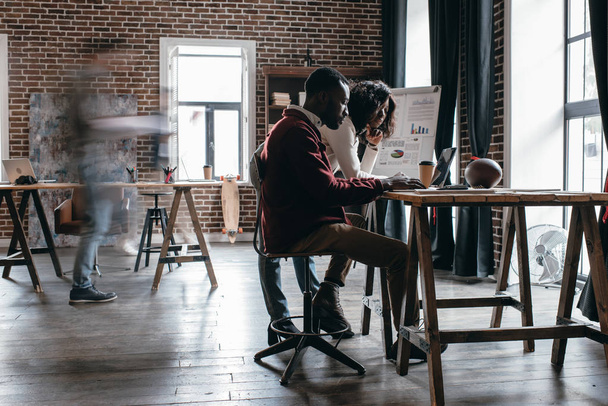 casal africano americano de empresários casuais que trabalham na mesa com colegas em borrão de movimento no escritório loft moderno
 - Foto, Imagem