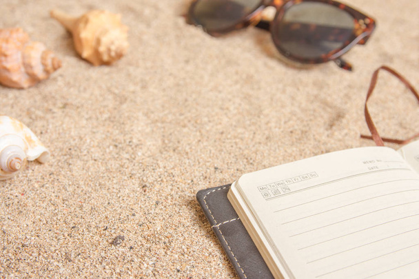 Personal planner and sunglasses on sandy beach closeup shot. - Фото, изображение