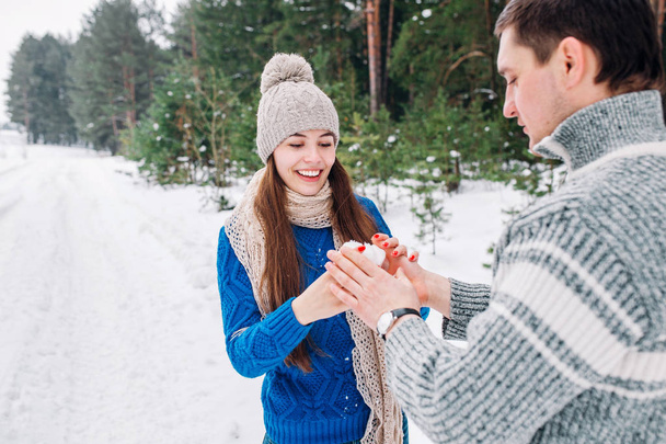 young couple holding snow heart in winter forest. Hands in knitted mittens with heart of snow in winter day. Love concept. Valentine day background. - Fotografie, Obrázek