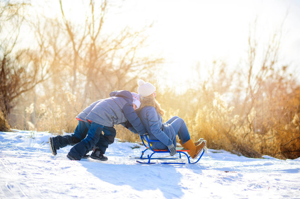 children play in the winter forest at sunset, the boys roll the girl on a sled - Foto, Imagem