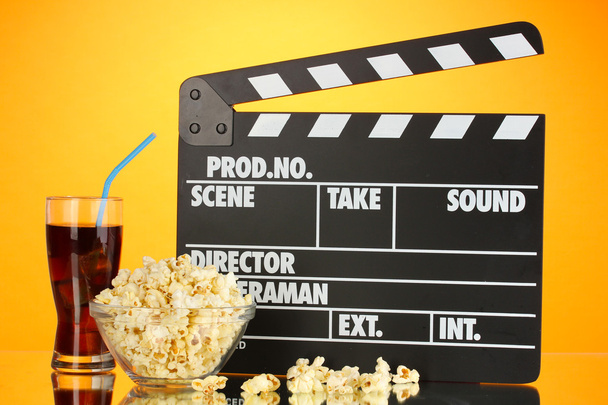 Movie clapperboard, cola and popcorn on orange background - Photo, Image