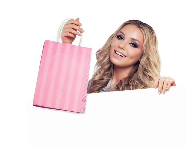 Cheerful woman with shopping bags and empty paper banner isolated on white background - Photo, Image