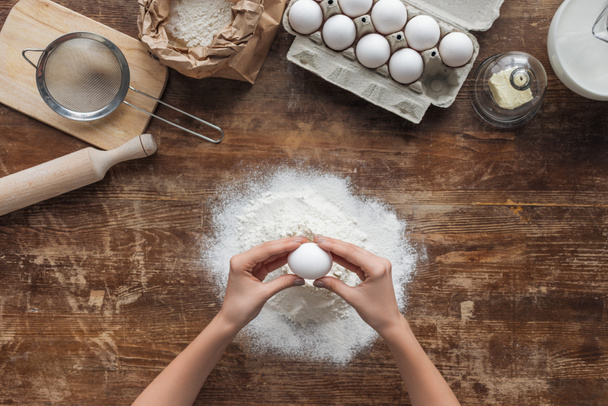 top view of female hands smashing egg in flour on wooden table - Valokuva, kuva