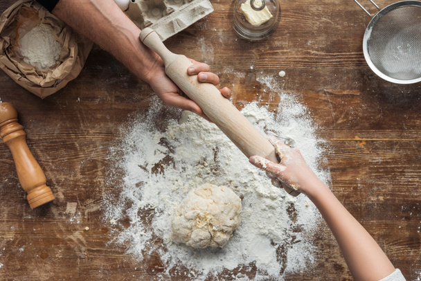 top view of cookers hands holding rolling pin above wooden table - Photo, Image