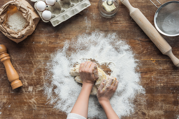 top view of female hands making dough on wooden table - Foto, Imagen