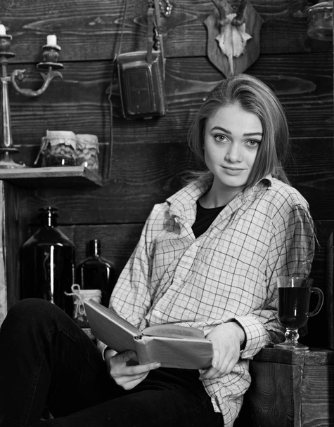 Study concept. Girl student study with book in house of gamekeeper. Lady on calm face in plaid clothes looks cute and casual. Girl in casual outfit sits with book in wooden vintage interior - Φωτογραφία, εικόνα