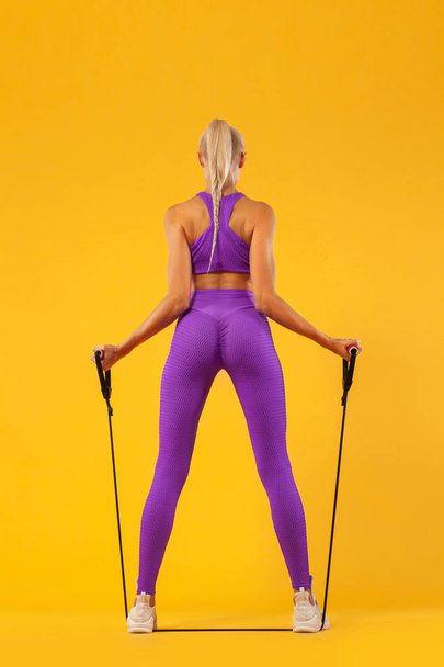 Fitness woman athlete and bodybuilder holding expander. Isolated on yellow background. - Valokuva, kuva