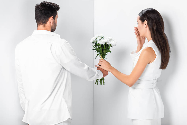 close up of man giving flowers to surprised woman in total white - Фото, изображение