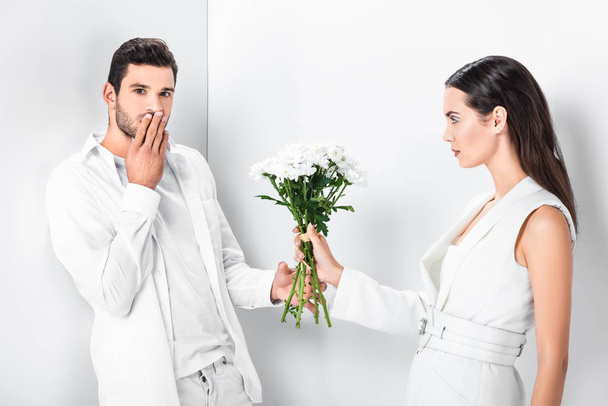 close up of beautiful woman in total white giving bouquet of flowers to surprised man  - Foto, immagini