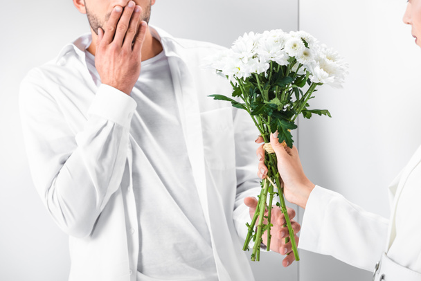 close up of woman in total white giving bouquet of flowers to surprised man  - Фото, изображение