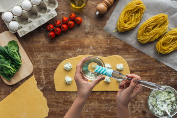 vue de dessus des mains féminines avec bol et pinceau à badigeonner cuisson ravioli au-dessus de la table en bois
 - Photo, image
