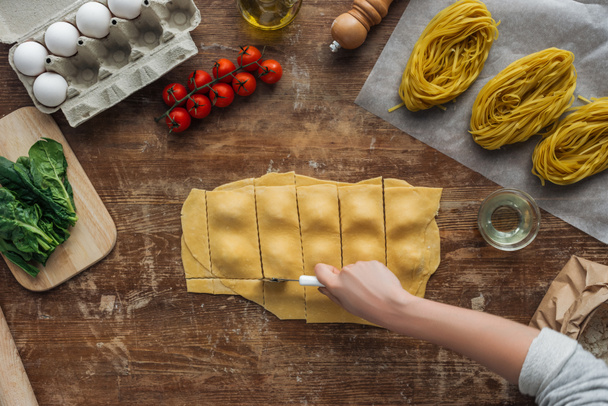 top view of female hands cutting out ravioli at wooden table - Фото, изображение