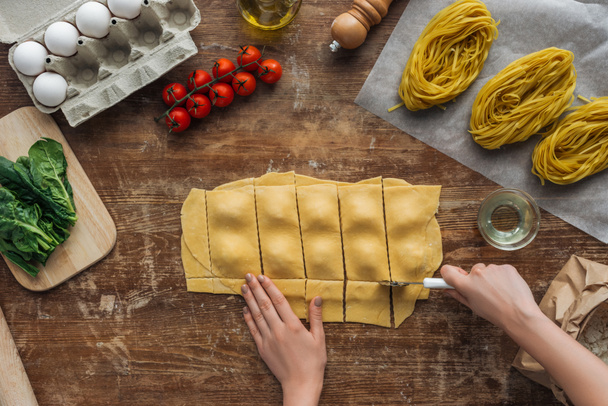 top view of female hands cutting out ravioli with pastry wheel at wooden table - Foto, imagen