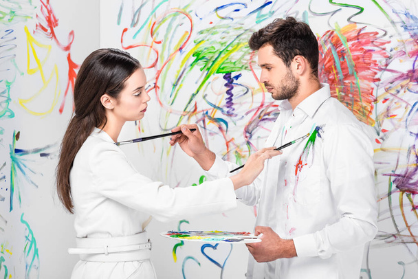 studio shot of couple in total white drawing on clothes with painbrushes - Fotó, kép