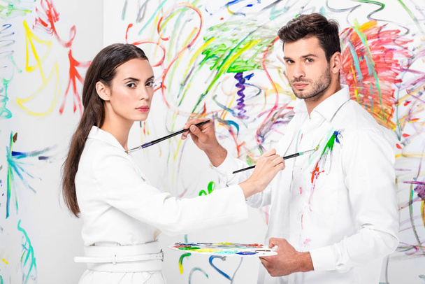 studio shot of couple in total white drawing on clothes with painbrushes - Fotoğraf, Görsel