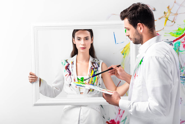 взрослая женщина, стоящая с белой рамкой, в то время как мужчина держит оборудование для рисования
 - Фото, изображение