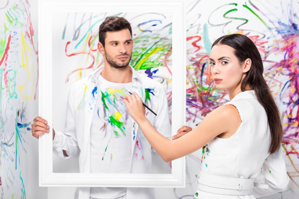 close up of adult man holding white frame while woman painting clothes - 写真・画像