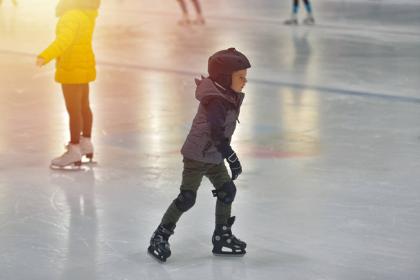 Roztomilý chlapeček v zimní oblečení s ochranami Bruslení na kluzišti - Fotografie, Obrázek