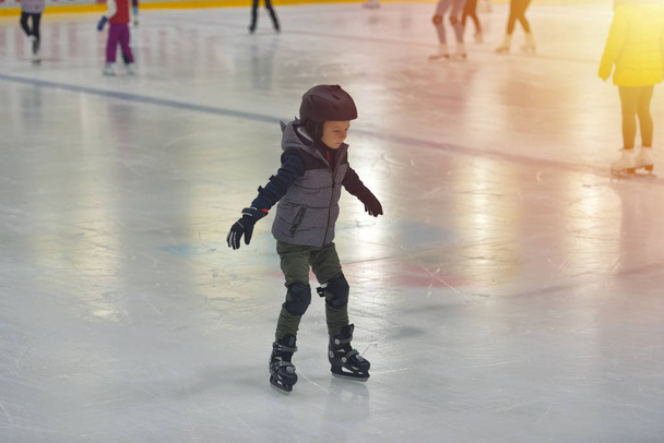 Очаровательный маленький мальчик в зимней одежде с защитой катания на катке
 - Фото, изображение