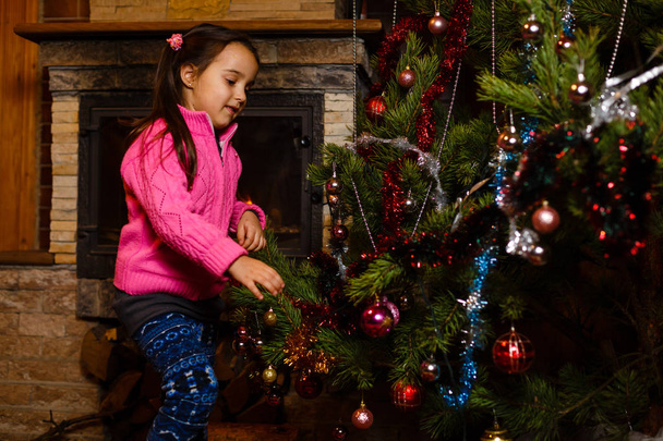Niña decorando árbol de Navidad con luz, bolas y bastones de caramelo
 - Foto, Imagen
