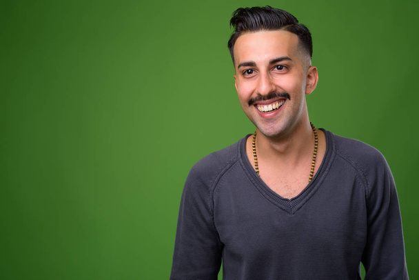 junger schöner iranischer Mann mit Schnurrbart vor grünem Hintergrund - Foto, Bild