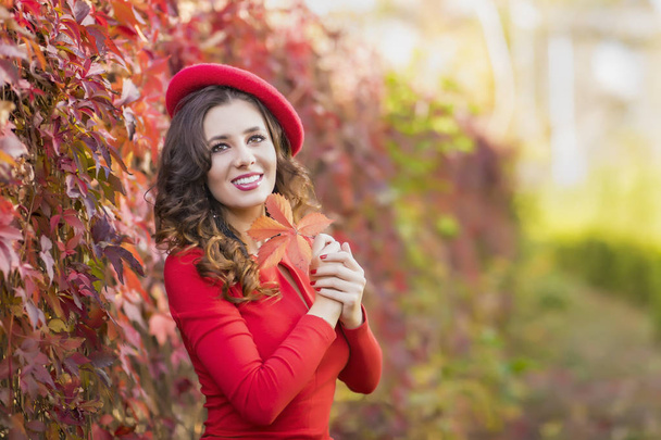Όμορφη νεαρή γυναίκα με κόκκινο φόρεμα σε μια ηλιόλουστη φθινοπωρινή μέρα - Φωτογραφία, εικόνα
