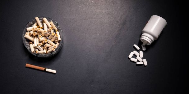 The concept of smoking and harm to health. An ashtray and a cigarette on a black board and white medical pills. May illustrate lifestyle choices. - Fotó, kép