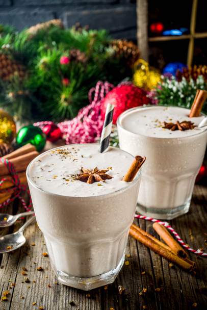 Χριστουγεννιάτικο γλυκό κρύο ποτό, σπιτικό eggnog milkshake σε δυο ποτήρια με κανέλα και γλυκάνισο, παλιό ξύλινο υπόβαθρο με Χριστουγεννιάτικες διακοσμήσεις αντίγραφο χώρου - Φωτογραφία, εικόνα
