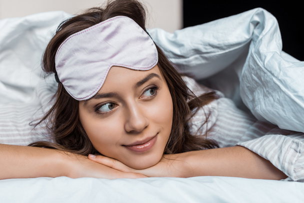 attractive girl in sleeping mask relaxing under blanket on bed   - Zdjęcie, obraz