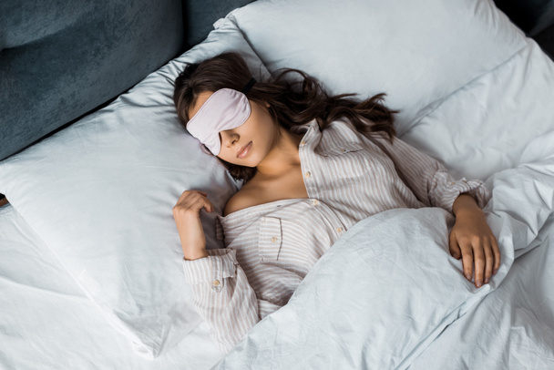 όμορφη νεαρή γυναίκα στον ύπνο με μάσκα ματιών στο κρεβάτι - Φωτογραφία, εικόνα