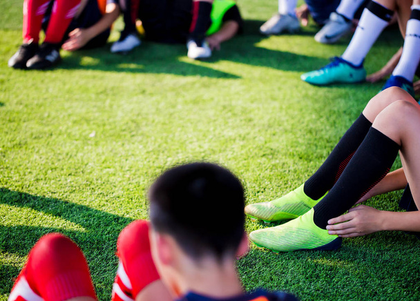 Ποδοσφαιριστές παιδί κάθονται με την υπερθέρμανση του πλανήτη στην Πράσινη τεχνητή τύρφη για τέντωμα μυών, πριν και μετά το παιχνίδι ποδοσφαίρου. Ποδόσφαιρο ή Ακαδημία Ποδοσφαίρου. - Φωτογραφία, εικόνα