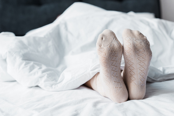 vista recortada de chica en calcetines acostado debajo de una manta blanca en la cama
 - Foto, imagen