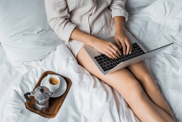 cropped view of woman with coffee using laptop in bed in the morning - Φωτογραφία, εικόνα