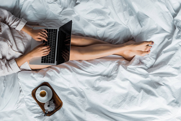 χαμηλή τομή της γυναίκας με Κύπελλο και moka μπρίκι χρησιμοποιώντας το laptop στο κρεβάτι - Φωτογραφία, εικόνα