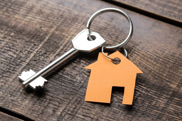 Концепция покупки дома. Ключи от брелока на коричневом деревянном фоне крупным планом
. - Фото, изображение