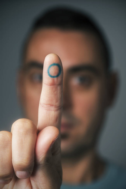 closeup of a young caucasian man with a blue circle, symbol of the diabetes, in his forefinger, in support of this disease - Foto, Bild