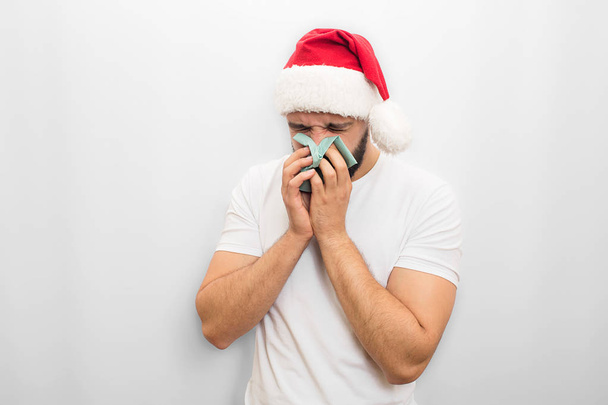 Sick young man in red hat stands and sneezes in napkin. He is ill. Guy in unhappy. Isolated on white background. - Φωτογραφία, εικόνα