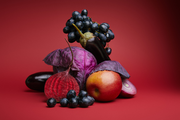 close-up view of fresh ripe grapes, apple, cabbage, beetroot, onion and eggplants on red background - Photo, Image