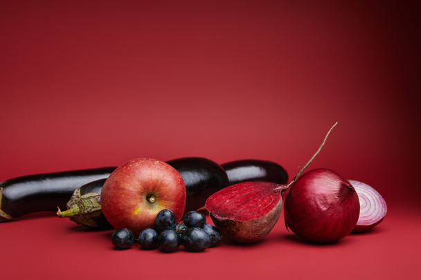 vista de cerca de manzana fresca, uvas, berenjenas, remolacha y cebollas sobre fondo rojo
 - Foto, Imagen