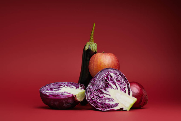 fresh ripe apple, eggplant, onion and sliced cabbage on red background - Foto, afbeelding