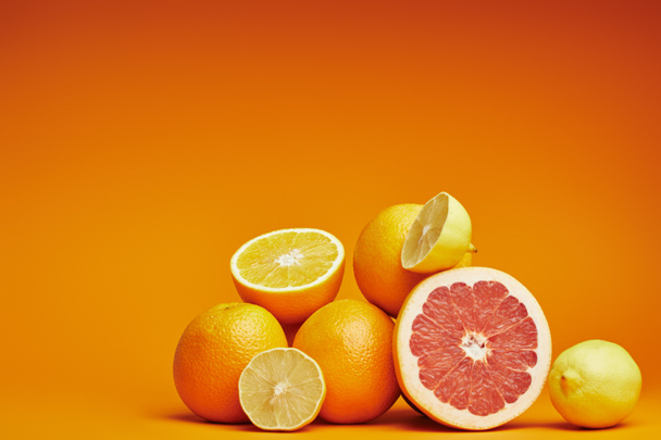 świeżych dojrzałych całe i krojone owoce cytrusowe na pomarańczowym tle - Zdjęcie, obraz