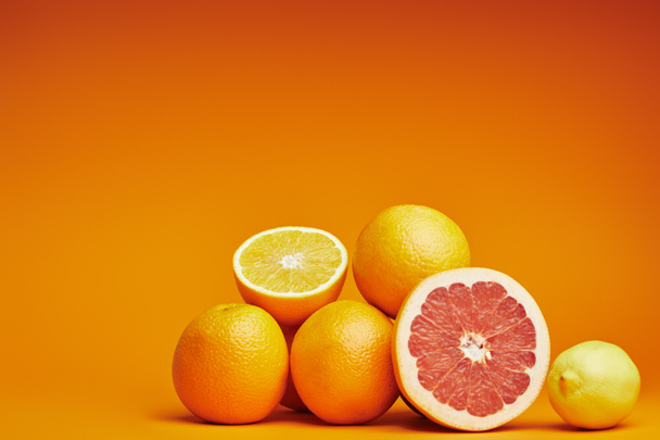 close-up view of fresh ripe whole and sliced citrus fruits on orange background - Photo, Image