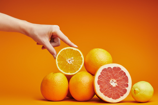 cropped shot of human hand and fresh ripe citrus fruits on orange - Photo, Image