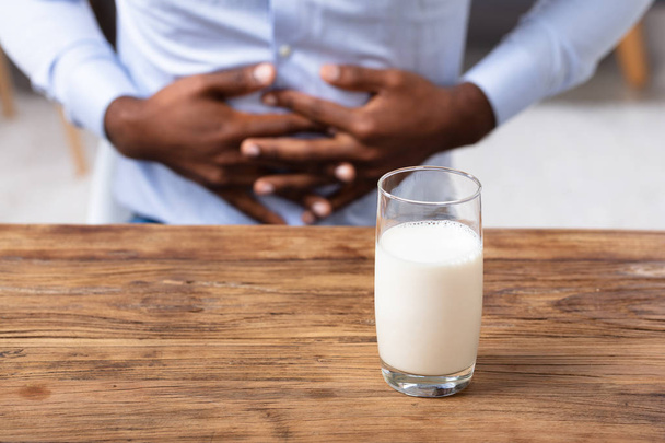 Glass Of Milk On Wooden Desk In Front Of Man Suffering From Stomach Pain - Foto, Bild