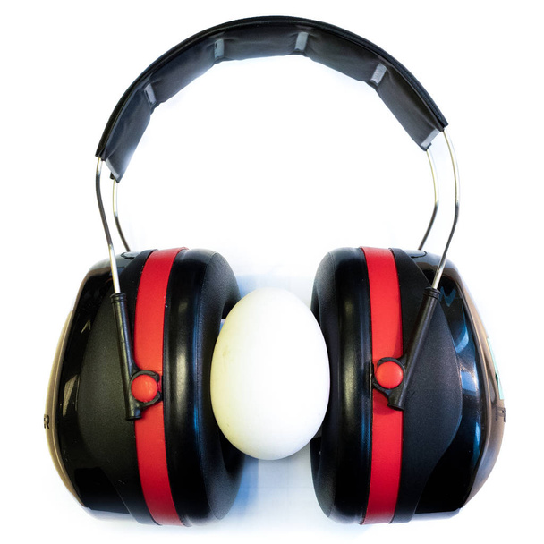 Fones de ouvido de proteção isolados em fundo branco com um ovo entre os auriculares
 - Foto, Imagem