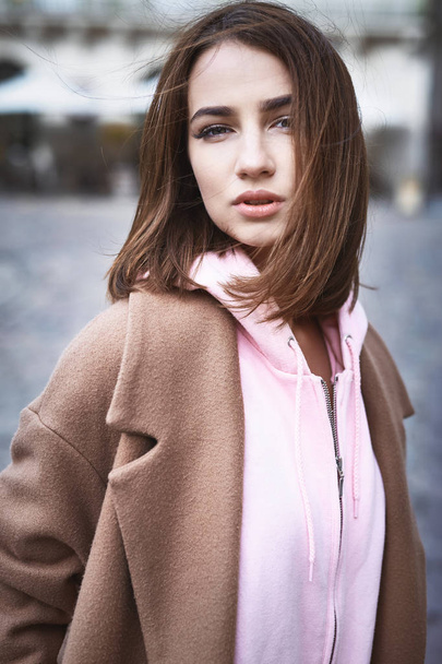 young woman in brown coat and pink hoody posing on the street - Foto, Imagem