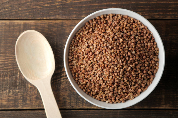 Semole secche di grano saraceno in una ciotola bianca con un cucchiaio su un tavolo di legno marrone. cereali. cibo sano. Porridge. vista dall'alto
 - Foto, immagini